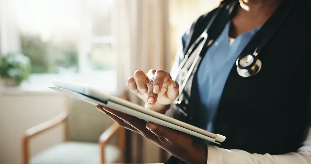 A practitioner with a stethoscope reviewing notes on a tablet