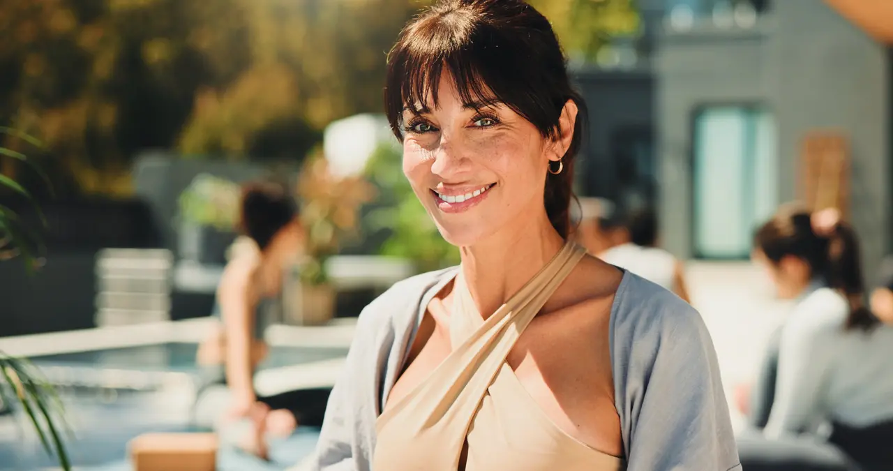A smiling woman in yoga wear at an outdoor wellness class