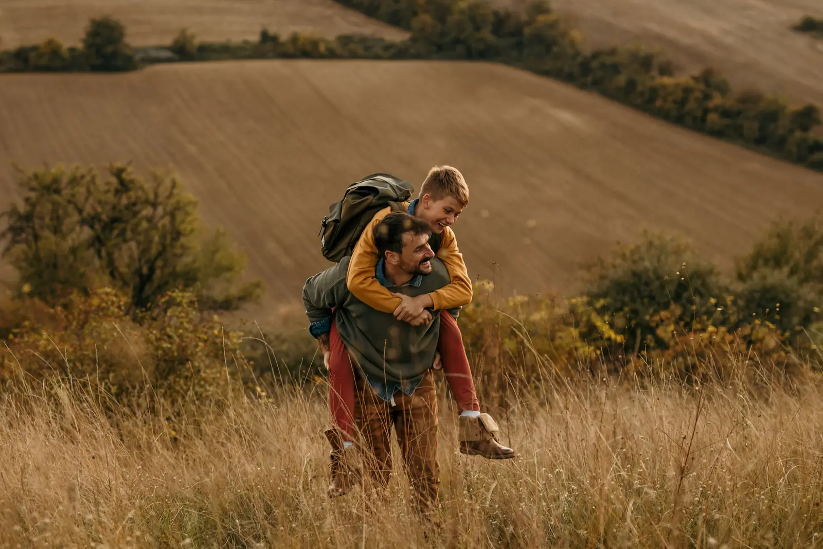 A father carrying his son on his back through a grassy field