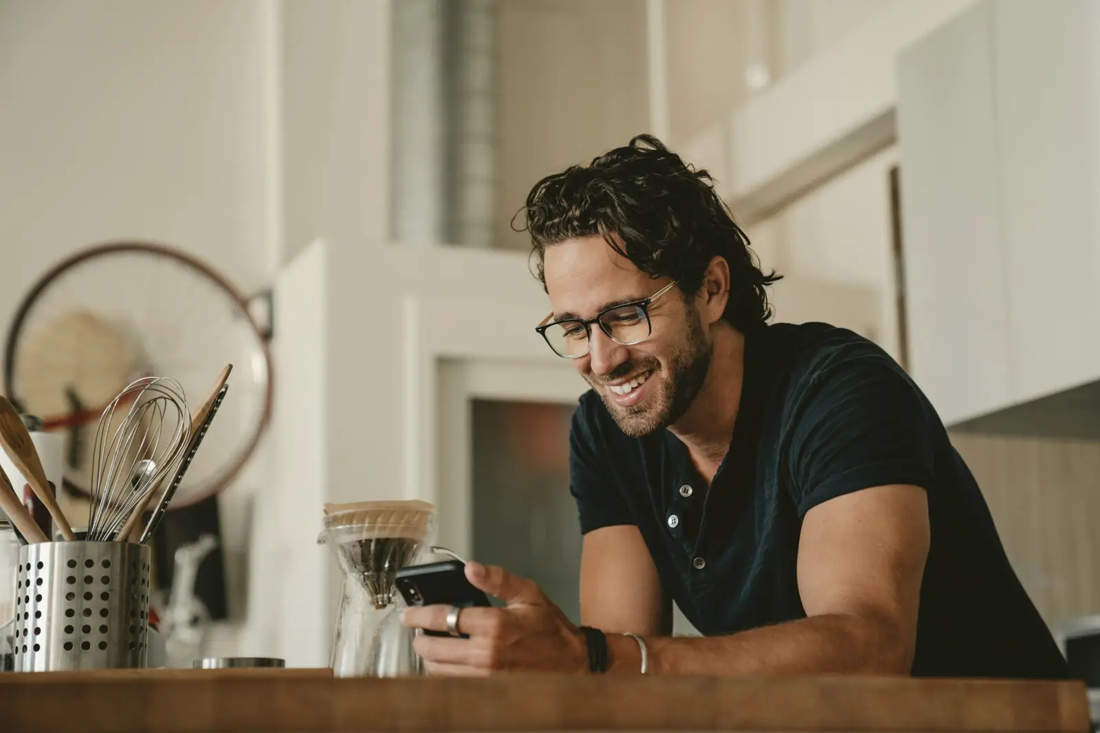 A man smiling at his phone in his kitchen