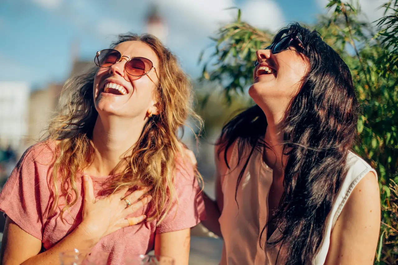 Two women laughing together outdoors on a sunny day