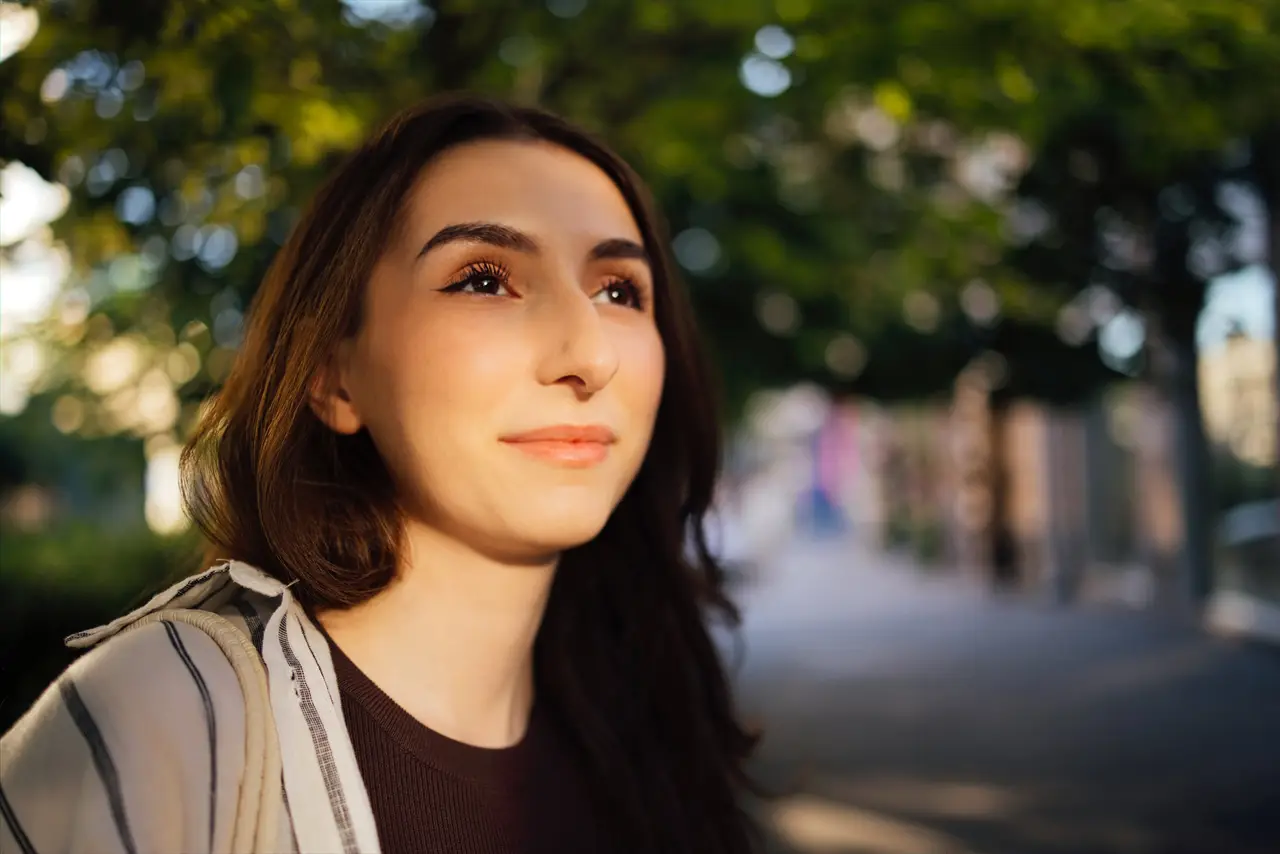 A young woman looking up thoughtfully in a sunlit, tree-lined street