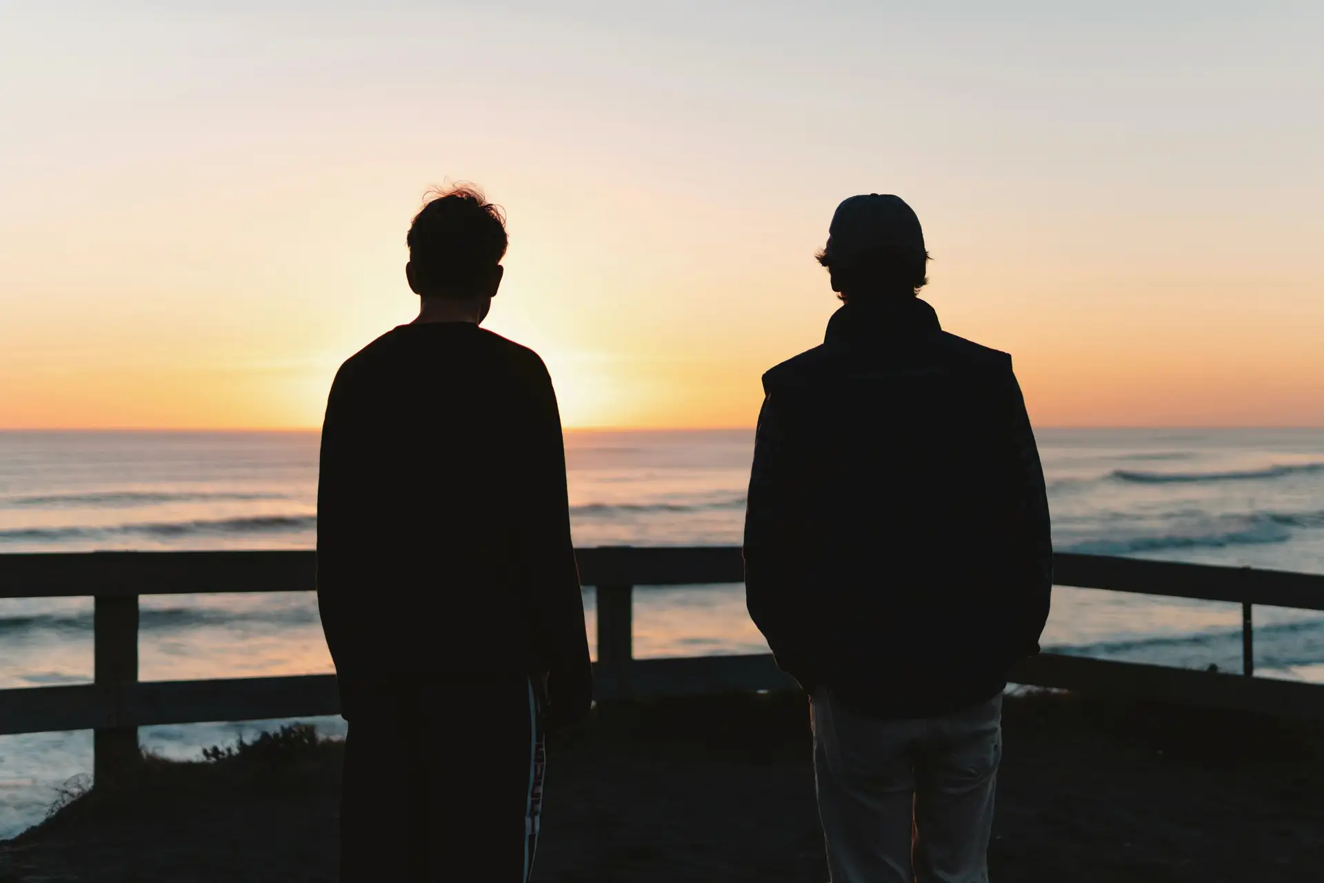 Two men silhouetted against a gold ocean sunset