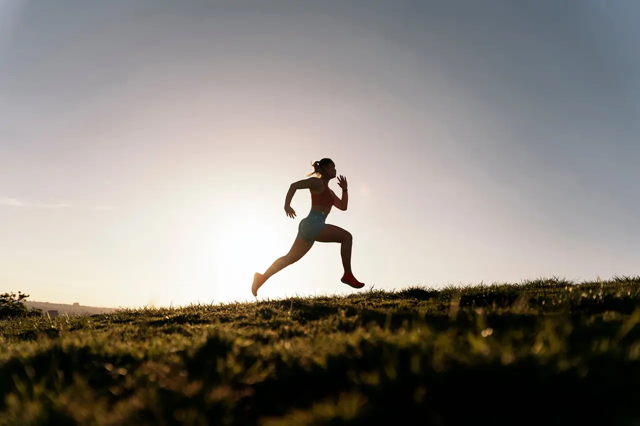 A woman running up a grassy hill against the sunrise